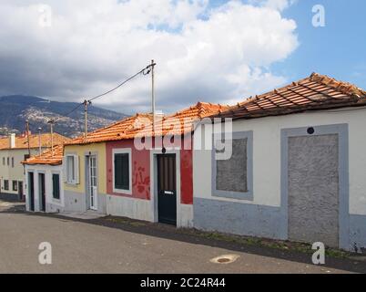 Eine Reihe von bunten alten gemalten einstöckigen untergebracht in einer schrägen Straße in funchal madeira in hellem Sonnenlicht mit blauem Himmel Stockfoto