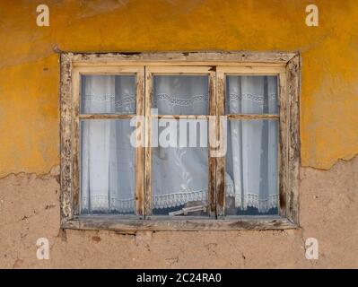 Holzfenster eines Hauses mit alten lehmziegeln. Ein Holzfenster mit weißem Vorhang. Außenansicht. Stockfoto
