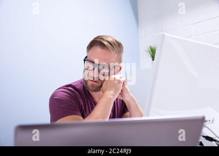 Unglückliche junge Mann sitzen vor dem Computer Monitor im Büro Stockfoto
