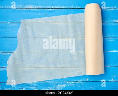 Abgewickelte Blättern von hellbeige Pergamentpapier auf einem blauen Hintergrund Holz, Ansicht von oben Stockfoto