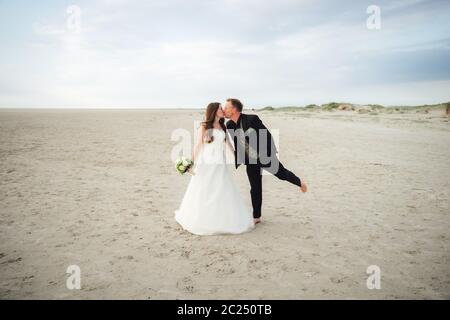 Brautpaar stehen und küssen sich am Sandstrand. Braut und Bräutigam posieren. Hochzeitskonzept. Stockfoto