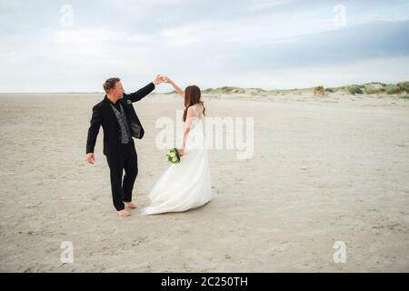 Frisch verheiratetes Paar tanzt am Sandstrand. Braut und Bräutigam schauen sich gegenseitig an und lächeln. Barfuß tanzen. Hochzeitskonzept. Stockfoto