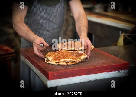 Gebackene Lahmacun ist ein rundes, dünnes Stück Teig, gekrönt mit Hackfleisch (am häufigsten Rind oder Lamm), gehacktem Gemüse und Kräutern. Mann schneidet lahmacun. Stockfoto