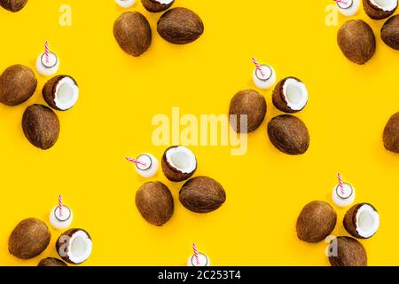Muster mit reifen Kokosnüssen und Flasche mit Getränk auf gelbem Hintergrund. Draufsicht. Kreatives Sommerkonzept. Exotische und tropische Erfrischung. Natürlicher Plan Stockfoto