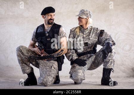 Die männlichen und weiblichen Militärs mit Waffen schauen sich auf grauem Wandhintergrund. Stockfoto