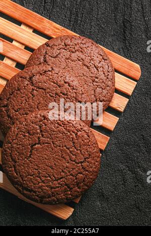 Drei Schokolade Haferflocken Cookies liegen auf einem Bambusblatt auf schwarzem Beton. Flach legen Draufsicht Stockfoto