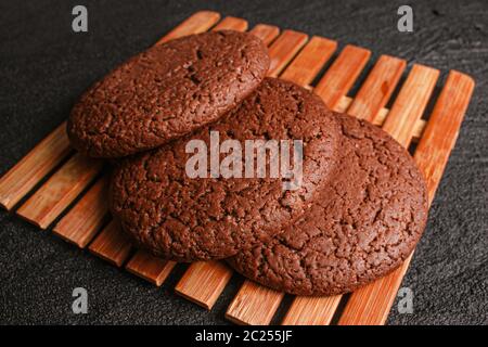 Drei Schokolade Haferflocken Cookies liegen auf einem Bambusblatt auf schwarzem Beton. Flach legen Draufsicht Stockfoto