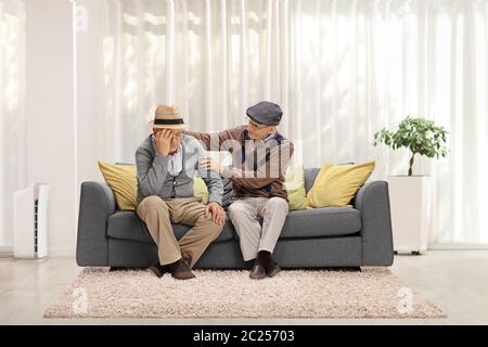 Älterer Mann tröstet seinen traurigen Freund und sitzt auf einem Sofa Stockfoto