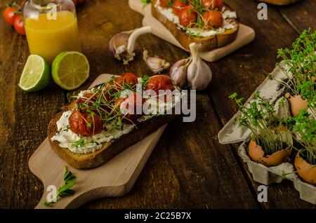 Geröstete Kirschtomatensoße und Ricotta auf Toast, frisch gepresster Orangensaft mit Limette, Bio-Knoblauch und Mikrogemüse auf Tomaten, gebacken mit Thymian Stockfoto