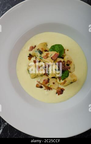 Spinat-Gnocchi mit Parmesan-Sauce, garniert mit Speck, reinigen dienen, Zutaten im Hintergrund Stockfoto