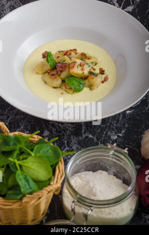 Spinat-Gnocchi mit Parmesan-Sauce, garniert mit Speck, reinigen dienen, Zutaten im Hintergrund Stockfoto