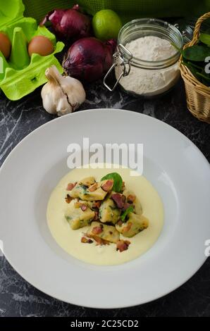 Spinat-Gnocchi mit Parmesan-Sauce, garniert mit Speck, reinigen dienen, Zutaten im Hintergrund Stockfoto