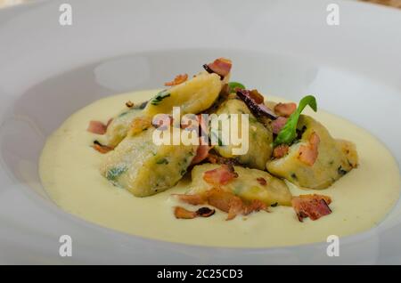 Spinat-Gnocchi mit Parmesan-Sauce, garniert mit Speck, reinigen dienen, Zutaten im Hintergrund Stockfoto