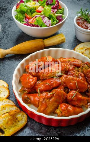 Heißen Hähnchenflügel mit würziger Habanero Sauce und gemischtem Salat mit Cherry-Tomaten, gegrilltes Baguette mit Olivenöl Stockfoto