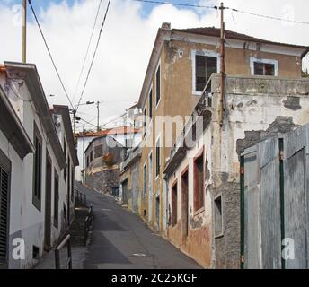 Eine schmale Hangstraße in funchal madeira mit alten portugiesischen Häusern mit Fensterläden und einem blauen, sonnenbeschienenen Himmel Stockfoto