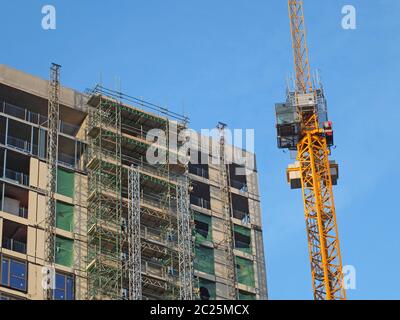 Großes modernes Gebäude im Bau, mit Gerüsten überzogen mit einem Turmkran gegen einen strahlend blauen Himmel Stockfoto