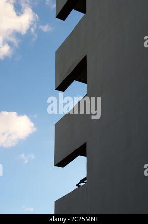 Die Ecke eines hohen Wohnhauses mit Balkonen bilden geometrische Formen gegen einen blau bewölkten Himmel Stockfoto