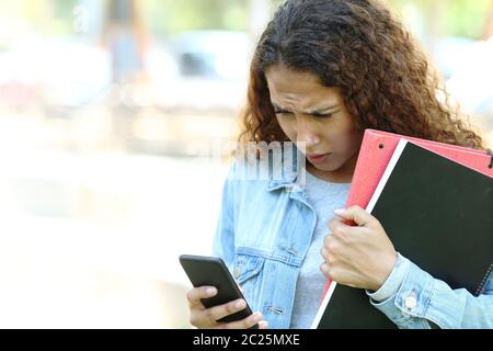 Traurig Mixed Race student prüfen smart phone Meldungen in einem Park oder Campus stehend Stockfoto