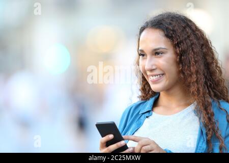 Gerne Frau auf der Suche nach gemischte Rasse holding Smart Phone zu Fuß auf der Straße Stockfoto