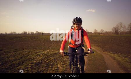 Sportliche kaukasische Frau isst Protein-Bar Fahrt auf dem Mountainbike auf der Natur. Junge sportliche Frau Athlet im Helm ruhen während bi Stockfoto