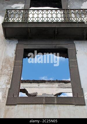Leere Fensterrahmen in einem überdachlosen Haus mit Balkon und weißen Innenwänden vor blauem Himmel Stockfoto