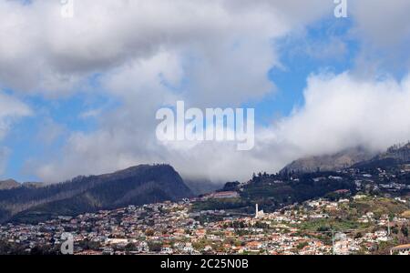 Ein Panoramablick auf funchal auf Madeira mit Häusern und Gebäuden gegen die baumbewachsenen Berge mit blauem Himmel und Wolken Stockfoto