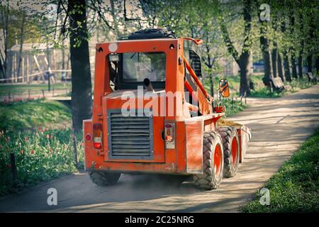 Orange Bulldozer mit einem Eimer bewegt sich entlang des Weges im Stadtpark Stockfoto