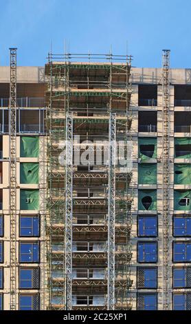 Modernes mehrstöckiges Apartmentgebäude im Bau mit Gerüsten und Hebebücken unter blauem Himmel Stockfoto