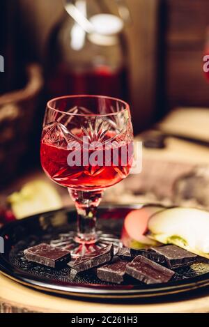 Glas hausgemachte rote Johannisbeere nalivka mit Apfelscheiben und Schokolade auf Metallplatte Stockfoto
