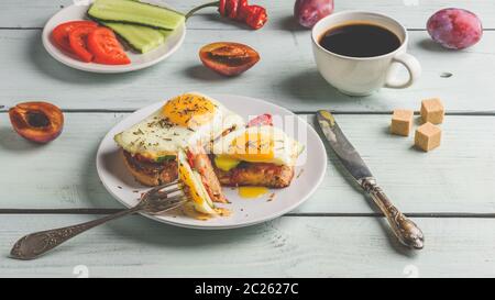 Sandwiches mit Gemüse und Spiegelei auf weissen Teller, Tasse Kaffee und einige Früchte über Holz- Hintergrund. Stockfoto