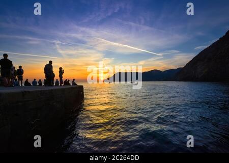 Touristen in Silhouette beobachten den Sonnenuntergang vom Hafen von Vernazza, Italien, an der ligurischen Küste der Cinque Terre Stockfoto