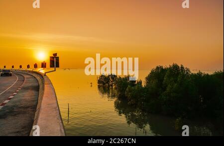 Geschwungene Küstenstraße und Auto mit orange Himmel bei Sonnenuntergang in Chonburi, Thailand. Stockfoto