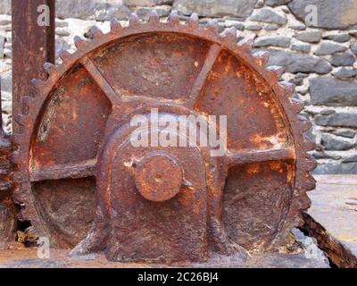 Ein großes altes rostiges Zahnrad auf veraltetem schweren Maschinenpark gegen eine Steinmauer Stockfoto