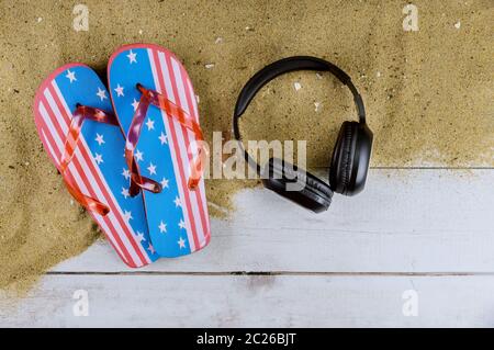 Amerikanische Flagge neue Flip-Flops Strand Hausschuhe Sand Strand Kopfhörer auf alten hölzernen Hintergrund Stockfoto