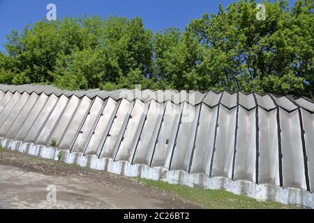 Industriehangar mit Aluminiumwänden und -Dach steht auf einem Betonfundament in der Nähe von grünen Bäumen Stockfoto