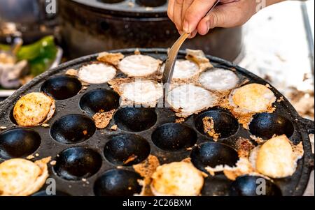 Mörtel - geröstete Gebäck oder "Kanom Krok' ist für traditionelle thailändische Dessert. Frau Hand entfernen Kanom Krok von Herd durch die Löffel. Street Food in Thailand. Thai d Stockfoto