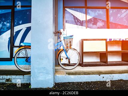 Fahrrad, das sich auf einen Stock in der Nähe eines hölzernen Schuhschrankes stützt, der auf einem Zementboden in einem Gebäude mit Fackellicht platziert ist. Vintage-Stil. Stockfoto