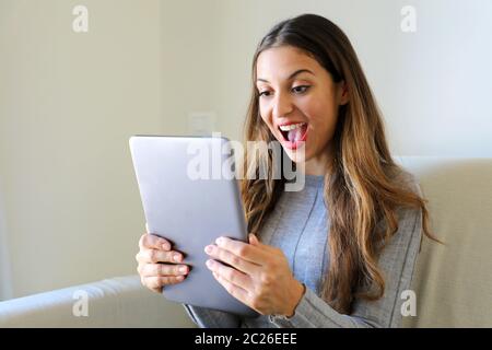 Glückliche Mädchen mit Tablet. Aufgeregt Frau hält Tablet-pc auf dem Sofa zu Hause Stockfoto