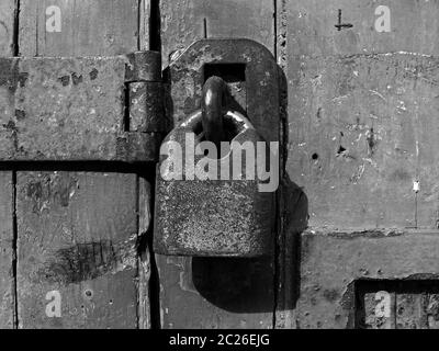 Monochrome Nahaufnahme eines alten rostigen geschlossenen Vorhängeschlosses und einer verzweifelten Holzbohlentür Stockfoto