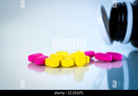 Gelb und Rosa, ovale Tablette Pillen mit Schatten auf weißem Hintergrund mit unscharfen Pillen Flasche. Leichte bis mäßige Schmerzen Management. Schmerzmittel Medizin. Stockfoto