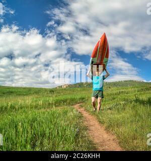 Ältere Paddler tragen ein langes Stand Up Paddleboard (SUP) bergab auf einem Trail im Frühsommer - Lory State Park, Colorado Stockfoto