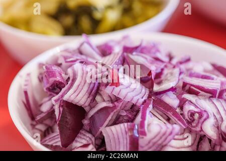 Nahaufnahme von Heap gehackte und geschnittene rote Zwiebel auf weißer Schüssel und rotem Tisch. Stockfoto