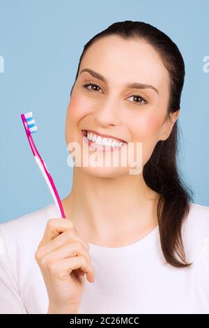 Schöne lächelnde Frau hält eine Zahnbürste auf blauem Hintergrund. Stockfoto