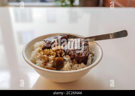 Nahaufnahme des Lu Rou Ventilator, Taiwanesische langsam kochen Sojasauce geschmorten Schweinebauch, mit Reis in der kleinen weißen Schale und weißer Tisch. Stockfoto