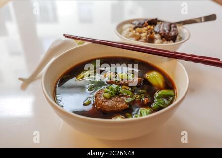 Taiwanesische Eintopf Rind Nudelsuppe ohne Nudel in weißer Schüssel auf weißem Tisch und verwischen Hintergrund der langsamen Koch Soja-Sauce Gebratenen Schweinefleisch Bauch, mit Reis. Stockfoto