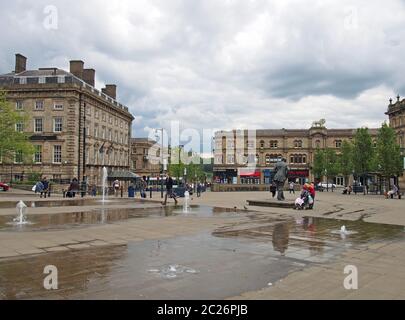 Menschen, die auf dem St. georges Platz in Huddersfield zwischen den Wasserbrunnen und den umliegenden Gebäuden spazieren Stockfoto