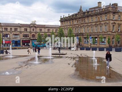 Menschen, die auf dem St. georges Platz in Huddersfield zwischen den Wasserbrunnen und den umliegenden Gebäuden spazieren Stockfoto