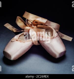 Pointe Shoes Ballet dance Schuhe mit einem Bogen der Bänder wunderschön auf einem dunklen Hintergrund gefaltet Stockfoto