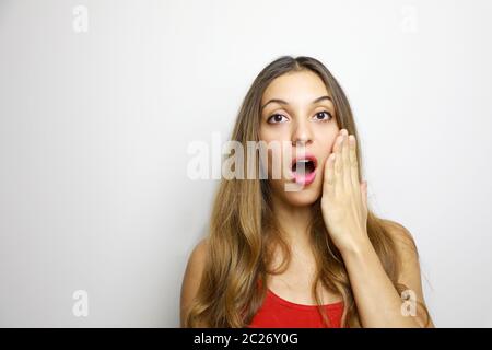 Überraschte Frau mit roten Lippen hält Wangen von Hand. Schönes Mädchen mit langen Haaren überrascht und schockiert schaut auf Sie. Präsentieren Ihres Produkts. Expres Stockfoto