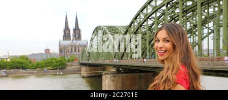 Glücklich lächelnde Frau, die ihre Reisen in Deutschland genießen. Schöne traveler Girl posiert vor der Kamera mit dem Kölner Dom und Hohenzollern Brid Stockfoto